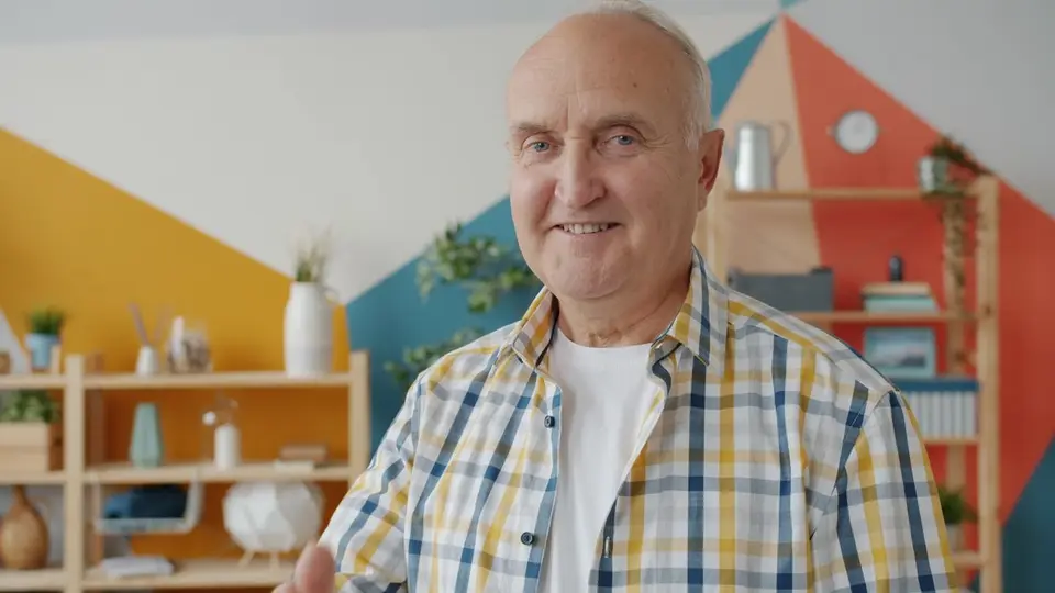 Friendly senior man smiling in a vibrant indoor setting with geometric patterns.