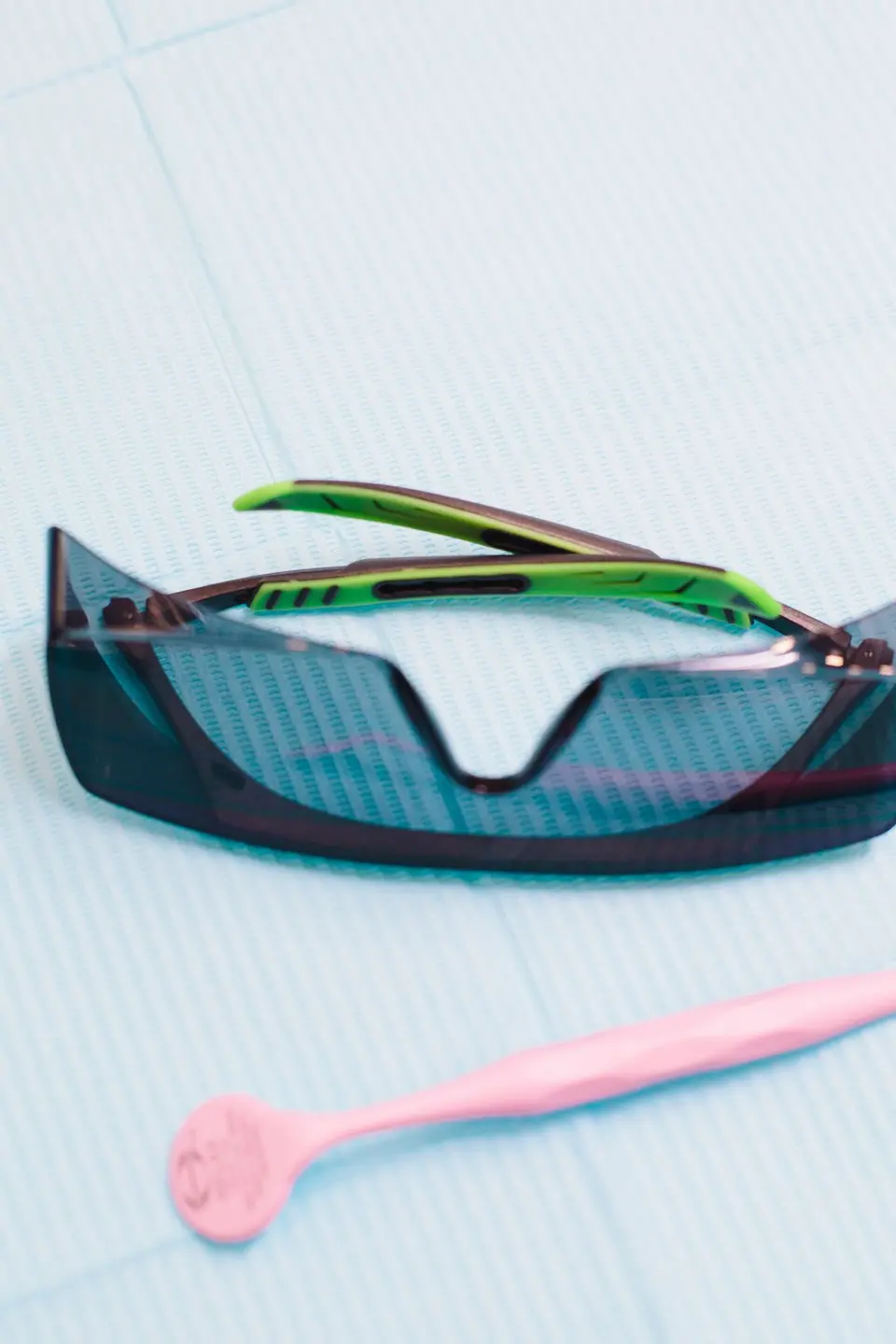 Close-up of dental goggles and a pink tongue scraper on a blue background.